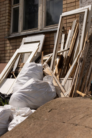 Piles of garbage and discarded construction materials are situated against a brick building. White...