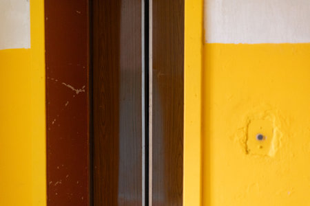 An elevator door in a deteriorating building with visible wear and peeling paint. The surrounding walls are painted in a contrasting yellow, highlighting the age and disrepairの写真素材