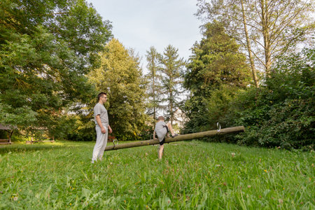 A father and his young child engage in playful activities at a playground, surrounded by vibrant greenery and trees, creating joyful memories in nature during the dayの写真素材