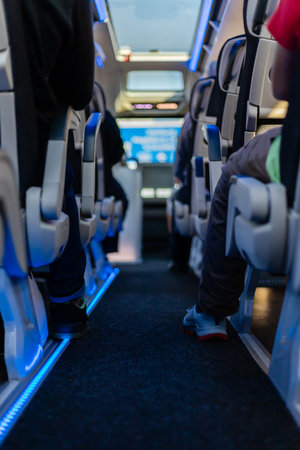 Inside a modern bus, passengers sit comfortably in spacious seats. Blue lights illuminate the aisle,...