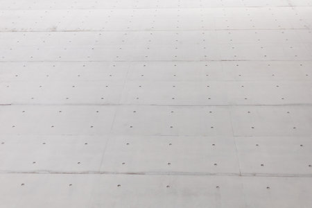 A close-up view of a concrete surface features evenly spaced holes. The setting suggests a construction area, illuminated by bright sunlight, highlighting the textureの写真素材