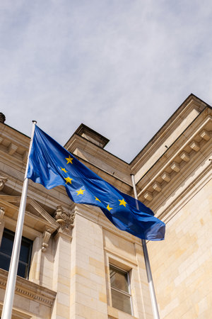 The European Union flag is displayed prominently on a flagpole in front of a grand historic...