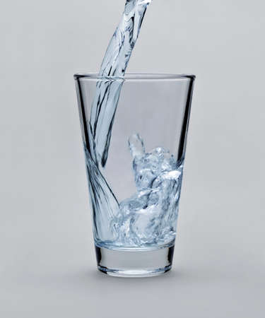 Pouring water into glass on light gray backgroundの写真素材