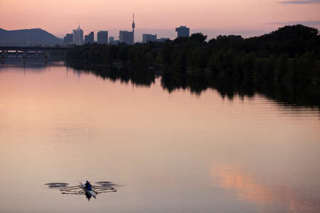 Rowing guys at dusk in the Danube River  Vienna-Austria  with urban skyline of the Danube City  UNO City, Donauturm, Leopoldsberg, etc   in the back の写真素材