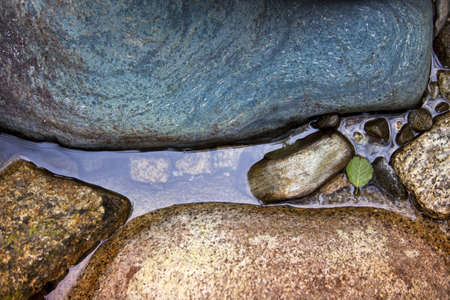 Body of water between gentle colored stones with one tiny green leaf 