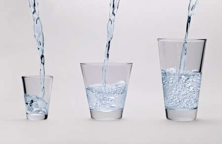 Pouring water into glasses on light gray background