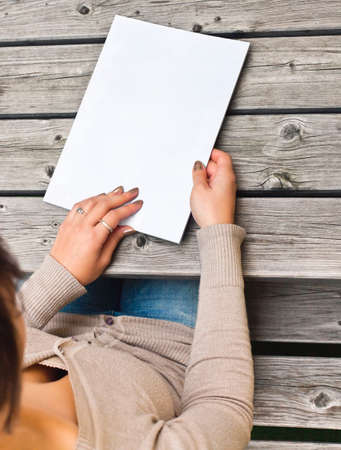 Young woman sitting at wooden table with a booklet with white cover The white cover can be used for any logos, label signs or any graphic additions の写真素材
