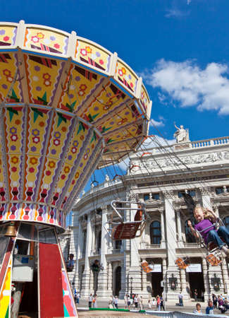Beautiful view of the historic Burgtheater (Imperial Court Theatre) at the famous Wiener Ringstrasse with some people enjoy a ride on a old-fashioned style Carousel on a sunny day in Vienna, Austriaのeditorial素材