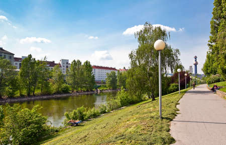 Some people relax at the pier of the Danube Canal located in the city center of Vienna with the Incineration Spittelau in the background.の写真素材