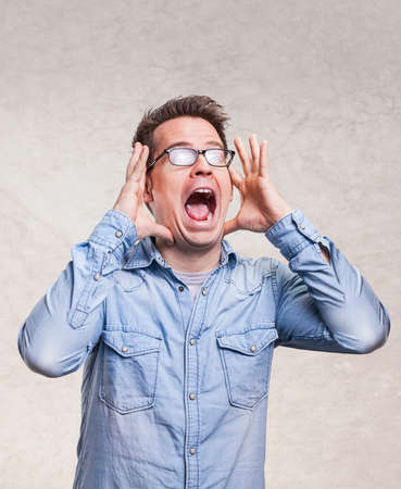 Portrait of a shocked, screaming, stunned or surprised young man holding head with his hands -  isolated on light gray wall backgroundの写真素材