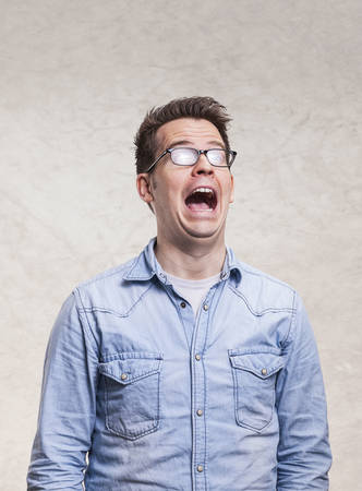 Portrait of a shocked, screaming, stunned or surprised young man - isolated on white light gray wall background.の写真素材