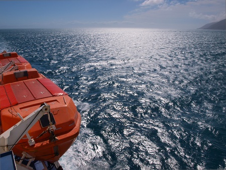a lifeboat on a the side of a ferry above a deep blue seaの写真素材