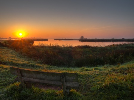 sunrise at the lake zuidlaardermeer with bench on foregroundの写真素材