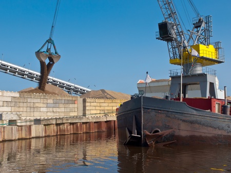 Yellow harbor crane is unloading sand from a ship in a dutch harborのeditorial素材