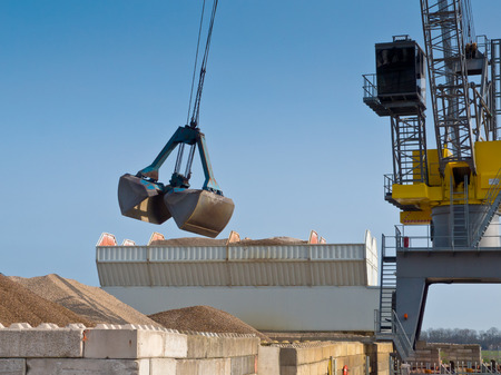 Yellow harbor crane is unloading sand from a ship into a silo