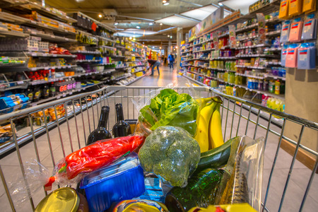 Grocery cart at a supermarket aisle filled up with food products seen from the customers point of viewの写真素材