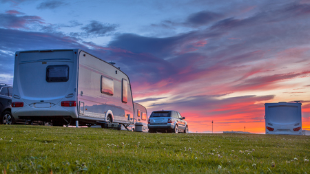 Caravans and cars parked on a grassy campground in summer under beautiful sunset