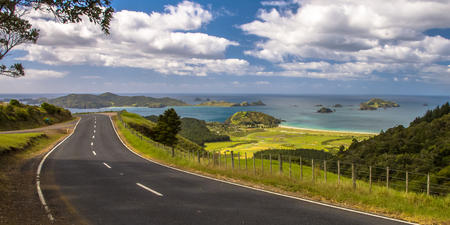 Inviting road through New Zealand countryside with blue sea with tropical islands at Bay of Islands, Northland, New Zealandの写真素材