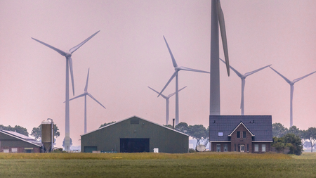 DELFZIJL, NETHERLANDS, JUNE 22 2017. Modern farm in open countryside with trees and wind turbines at orange sunsetのeditorial素材