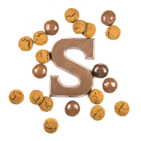 Chocolate letter S with bunch of scattered chocolate pepernoten cookies from above on white background for annual Sinterklaas holiday event in the Netherlands on december 5thの写真素材
