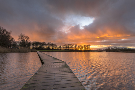 Wooden walkway in lake under orange sunset in december. Drenthe, The Netherlandsの写真素材