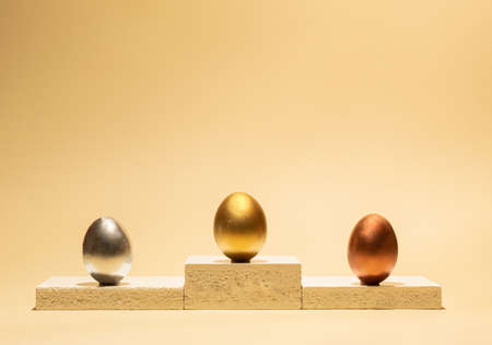 Three eggs standing on a winning podium during the awarding of gold, silver and bronze medals. Creative minimal 2021 Easter concept with copy space.の写真素材