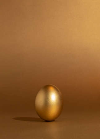 Golden and shiny Easter egg on monochromatic background. Modern Easter minimalistic contemporary style 2021. Minimal success concept.の写真素材