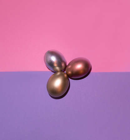 Three metallic shiny Easter eggs on pastel pink and purple background. Modern 2021 Easter concept....