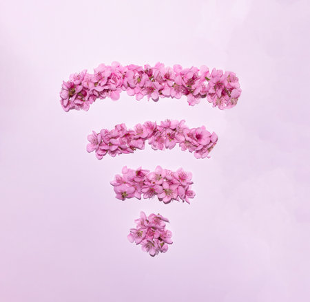 Wireless internet symbol concept made of spring flowers shaped into WiFi symbol on bright pink background. Minimal internet technology idea. Flat lay spring composition.の写真素材
