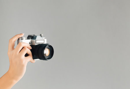 Old photo camera in woman hand on grey background with vintage color effect. Minimal retro style. Copy space.の写真素材
