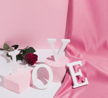 Romantic pastel pink Valentine's Day composition with word Love, satin curtain and red rose flower. Modern aesthetic. Minimal love concept.の写真素材