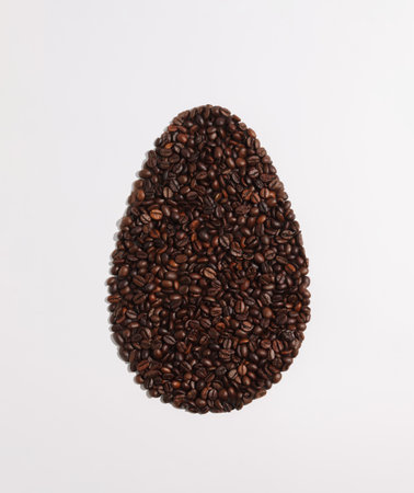 Easter egg shape made of coffee roasted beans on white background. Flat lay, top view. Minimal...