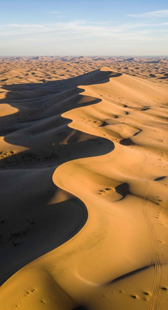Aerial view of vast desert with rolling golden sand dunes and clear blue sky