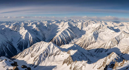 Aerial view of rugged, snow-covered mountains under a blue sky with scattered white clouds.