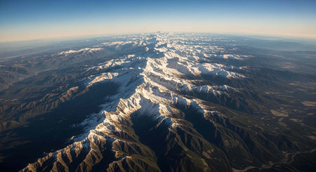 Panoramic aerial landscape of rugged snow-covered mountains with clear blue sky and sunlight casting...