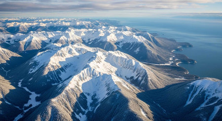 Aerial view of rugged snow-covered mountains meeting a vast ocean under a cloudy sky