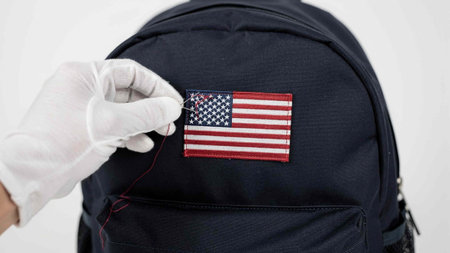 Close-up of a male hand in a white glove holding a small black backpack with the flag of the USA