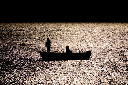 Silhouette of boat fishing in the sea in moonlight reflection reverse lightの写真素材