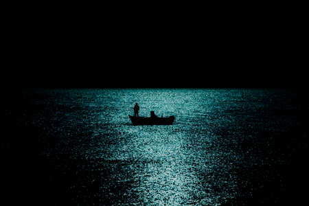 Silhouette of boat fishing in the sea in moonlight reflection reverse lightの写真素材
