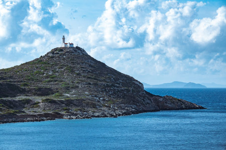 Rocky hilltop lighthouse with white walls and red roof under clear skies.の写真素材
