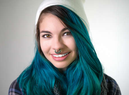 Beautiful smiling girl looking straight at camera. Pierced, turquoise haired and dressing up a white cap.の写真素材