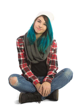 Beautiful serene girl sitting cross-legged and looking straight at camera. Pierced, turquoise haired and dressing up a plaid jacket and blue jeans.の写真素材