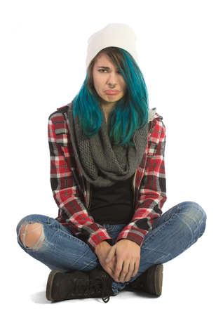 Sad and unhappy girl sitting cross-legged and looking straight at camera. Pierced, turquoise haired and dressing up a plaid jacket and blue jeans.の写真素材
