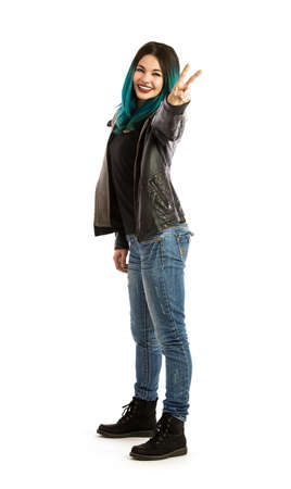 Smiling girl showing the peace sign on a white background. Pierced, turquoise haired, dressing a leather jacket and denim jeans.の写真素材