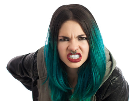Angry pierced girl looking straight at camera on a white background. Pierced, turquoise haired and dressing a leather jacket.の写真素材