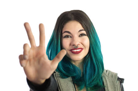 Smiling girl showing the three fingers, counting hand sign on white background. Pierced and turquoise haired.の写真素材