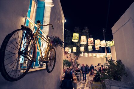 Decorative bicycle in a street of Chora Naxos and people eating in a typical Greece restaurant, Cyclades archipelago Greece - Imageの写真素材