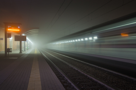 Railway platform without people waiting, with train hurtling into the foggy night.の写真素材
