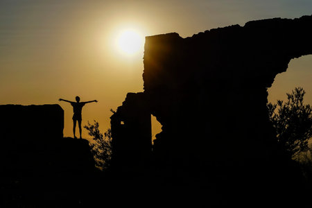 woman in a backlit ruins with the sun over the horizon