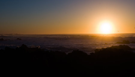 A colorful misty beach sunset with silhouetted rocks in the foregroundの写真素材